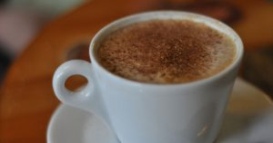 coffee with foam in a white cup on a white saucer with ground nutmeg on top