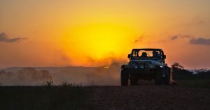 a jeep wrangler driving through the dirt at sunset