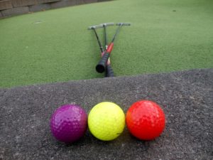 mini golf clubs with mini golf balls | golf balls in purple, yellow, and red on putting green